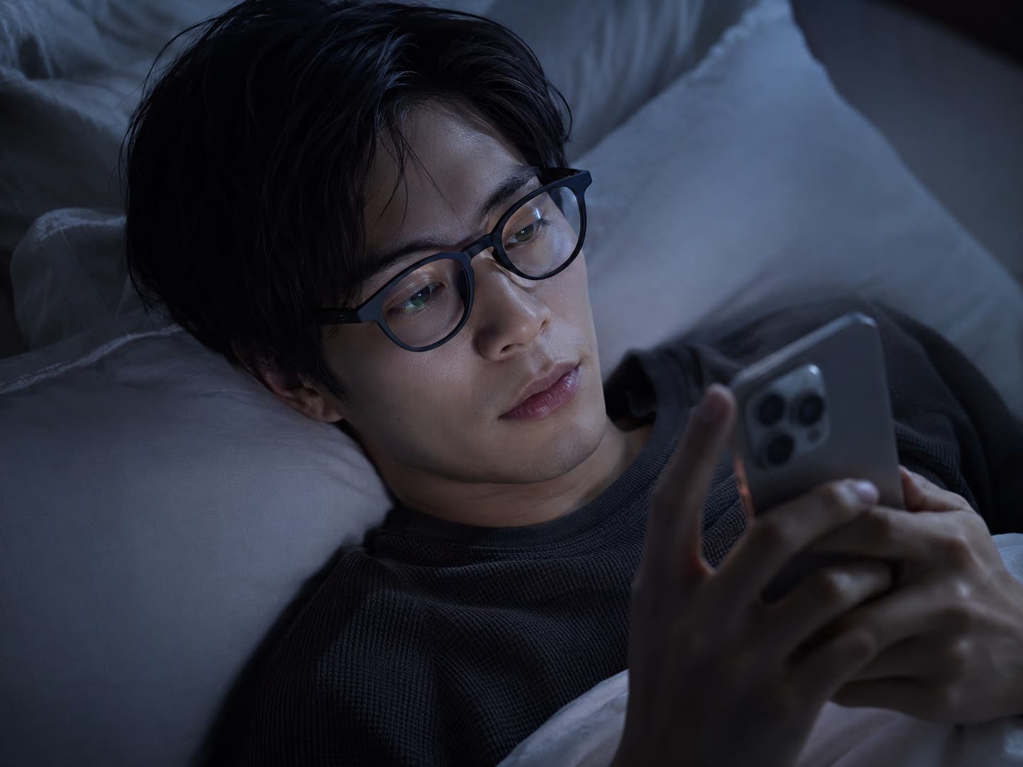 就寝前にベッドでスマートフォンを見るメガネの男性